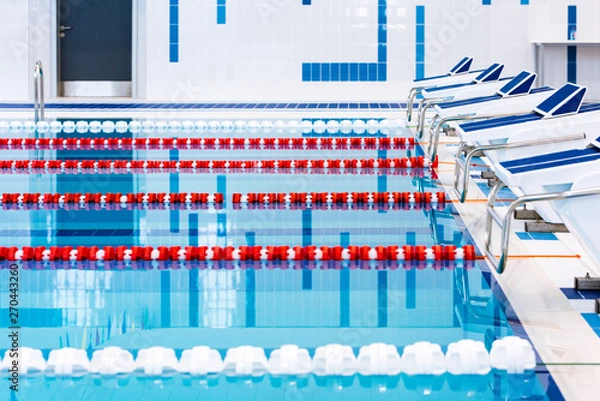 Fototapeta Swimming pool with marked red and white lanes. Empty swimming pool without people with quiet standing water. Water sports in indoor pool.