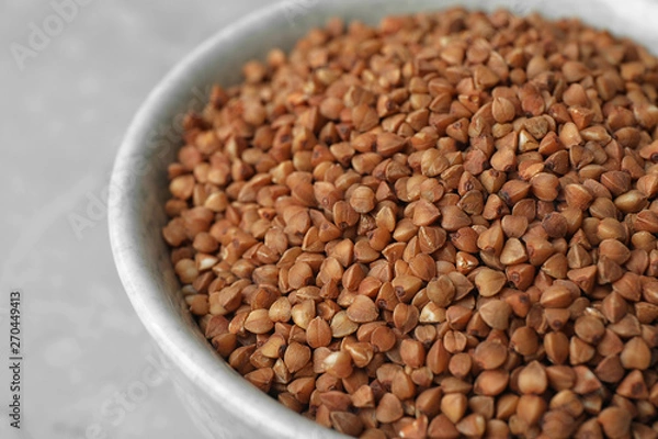 Fototapeta Uncooked buckwheat in bowl on table, closeup