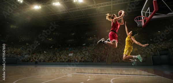 Fototapeta Female basketball players fight for the ball. Basketball player makes slam dunk on big professional arena during the game