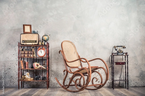Obraz Rocking chair, old telephone, broadcast radio, retro camera, frame blank, globe, books, antique binoculars, alarm clock, carnival mask, golden key, souvenirs on shelf. Vintage style filtered photo