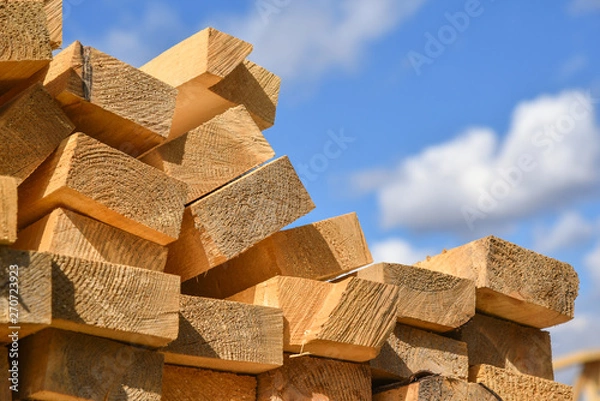 Fototapeta Stacked lumber on blue sky.Folded wood.Closeup wooden boards.The surface of the end of the board.Lots of planks stacked on top of each other in the warehouse.Lumber for use in construction.