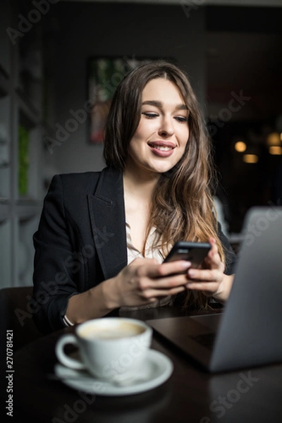 Fototapeta Smiling woman in cafe using mobile phone and texting in social networks.
