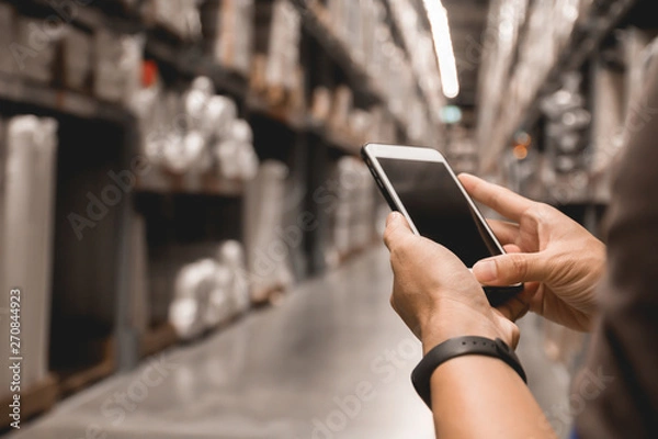 Fototapeta Close up business man hand holding blank screen mobile smart phone checking and contacts business logistics with warehouse background wholesale factory warehouse management, smart logistic, business, 