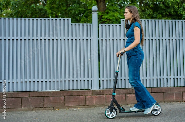Fototapeta Outdoor portrait of young teenager brunette girl with long hair driving scooter on city street
