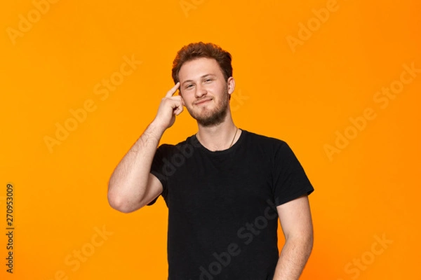 Fototapeta Studio shot of a bearded young man pointing a finger at the temple. Concept of a positive thinking.