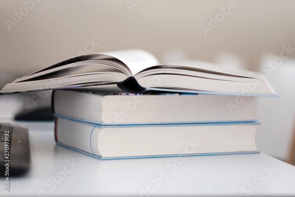 Fototapeta Open book on a stack of books on a table.
