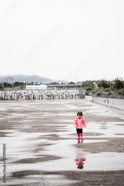 Fototapeta Child dressed in pink clothes jumping in puddles