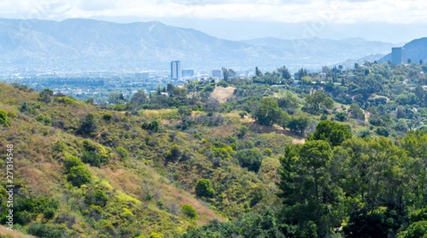 Obraz lush green rolling hills with the city of Los Angeles in the distance under hazy skies