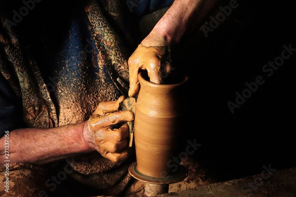 Obraz Close up mud covered hands of adult man making clay pot on potter's wheel