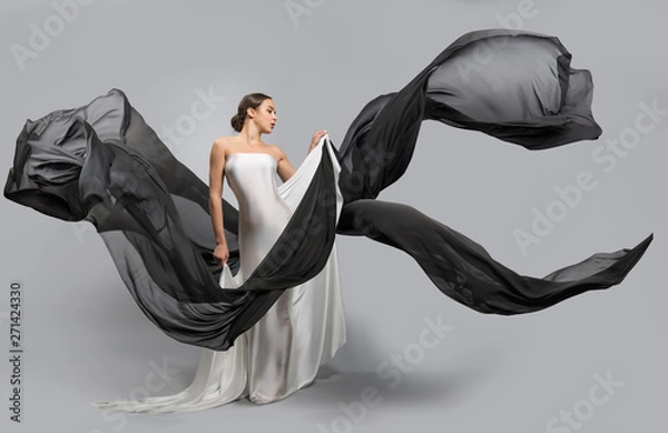Obraz fashion portrait of a beautiful woman in a white and black dress. The fabric flies in the wind.