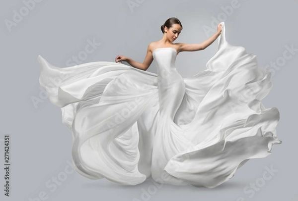 Obraz Fashion portrait of a beautiful woman in a waving white dress. Light fabric flies in the wind.