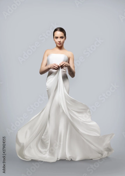 Obraz beautiful woman in a light fluttering white dress. Light fabric flies in the wind. Light gray background.