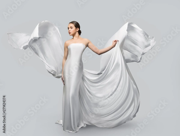 Obraz Fashion portrait of a beautiful woman in a waving white dress. Light fabric flies in the wind.