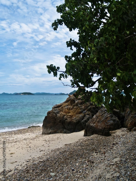Fototapeta The view of the sea with green leaves, sand gravel and large rocks and sky.