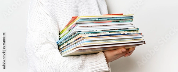 Fototapeta Girl in a white woolen sweater holding a stack of children's books on white background with copy space. Long wide banner