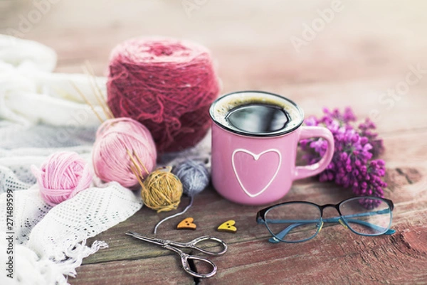 Fototapeta  Women's hobby. Crochet and knitting. Working space. Bouquet of lilac in a cup, balls of yarn, needles, scissors, knitwear, crochet hooks on the wood table  in the cozy home. 