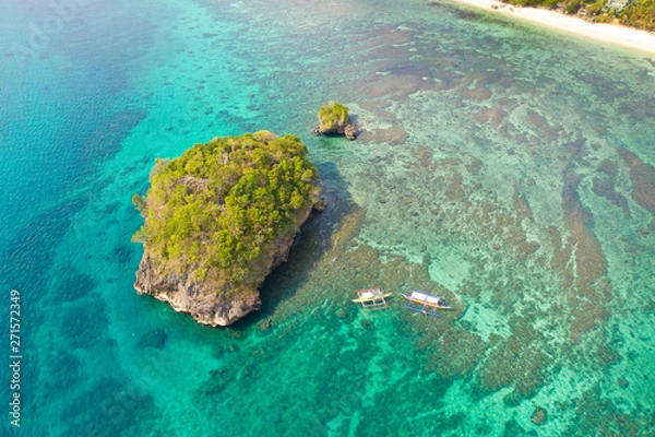 Fototapeta Small rocky island in the blue lagoon, view from above. Bay with turquoise water and coral bottom.