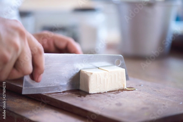 Fototapeta chef has a kitchen knife in his hand and cuts the tofu in a square shape