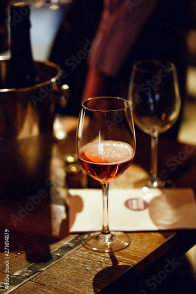 Fototapeta Moscow, Russia-March 30, 2019: Wine tasting. On the wooden table is a glass filled with pink champagne, a bucket for cooling bottles, brochures and empty wine glasses.