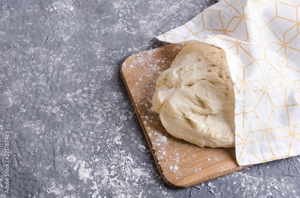 Fototapeta Closeup of dough under the napkin on the wooden board.Process of rising dough, empty space for your design