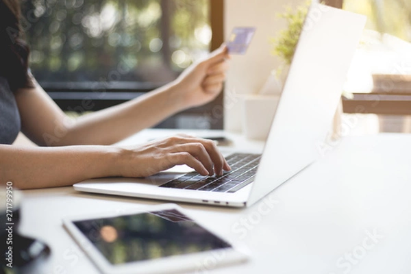 Fototapeta Hands of a beautiful woman holding a smartphone with a credit card ready to be online shopping.