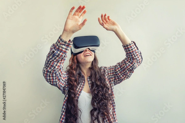 Fototapeta Smile young woman wearing using virtual reality VR glasses helmet headset on white background. Smartphone using with virtual reality goggles. Technology, simulation, hi-tech, videogame concept