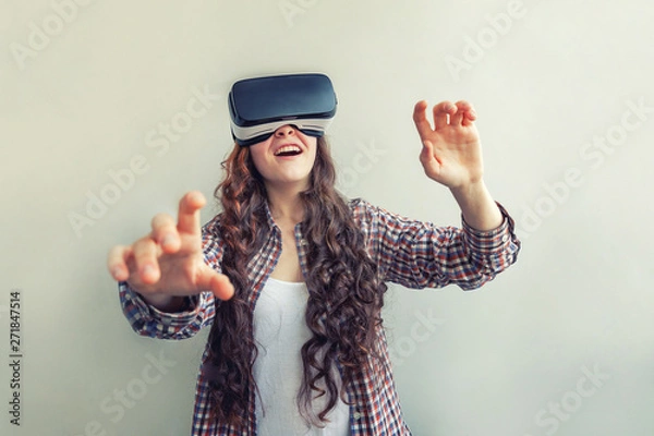 Fototapeta Smile young woman wearing using virtual reality VR glasses helmet headset on white background. Smartphone using with virtual reality goggles. Technology, simulation, hi-tech, videogame concept
