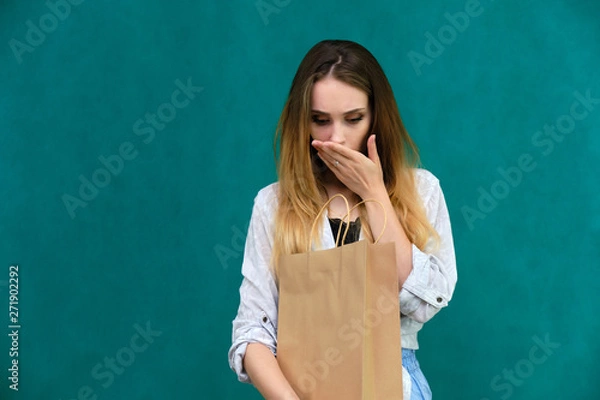 Fototapeta Photograph of a portrait of a beautiful girl woman with long dark flowing hair, loves shopping, on a green background with packages from the store. She is standing in different poses and smiling.