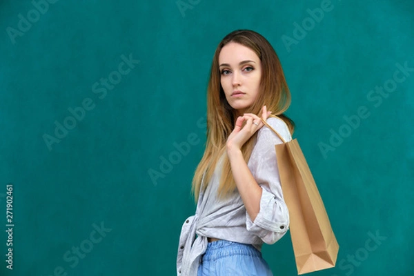 Fototapeta Photograph of a portrait of a beautiful girl woman with long dark flowing hair, loves shopping, on a green background with packages from the store. She is standing in different poses and smiling.