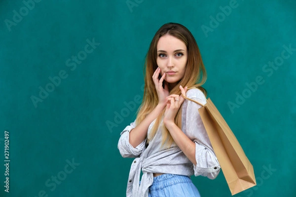 Fototapeta Photograph of a portrait of a beautiful girl woman with long dark flowing hair, loves shopping, on a green background with packages from the store. She is standing in different poses and smiling.