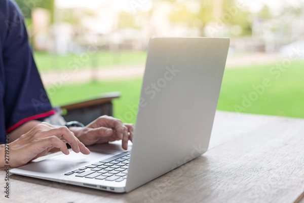 Fototapeta Woman hand using laptops and has a notebook and a pen with warm light