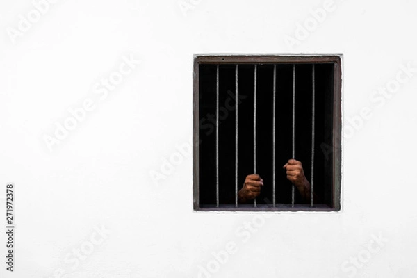 Fototapeta Hands of the prisoner on rusty bar of the window and prison cell white cement wall
