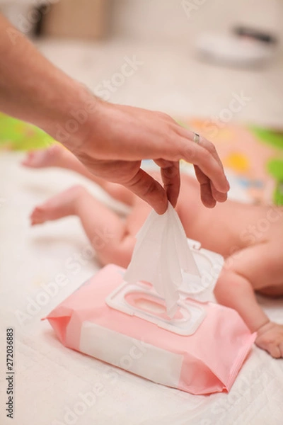 Fototapeta close up male hand pulls out a wet napkin. daily children's hygiene. paternity concept. newborn lying on his stomach in selective focus on the background