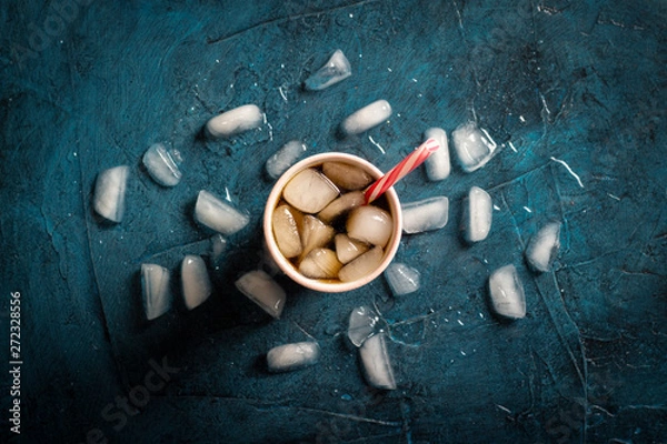 Fototapeta Iced coffee in a glass on a dark blue stone background with ice cubes. Concept cooling drink, thirst, summer, cola with ice, nightlife, club. Flat lay, top view