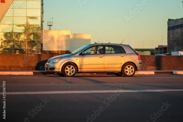 Fototapeta Deep morning dawn with highlights in the orange rays of the summer sun on the road with car against the background of industrial structure. Toned in orange colour.