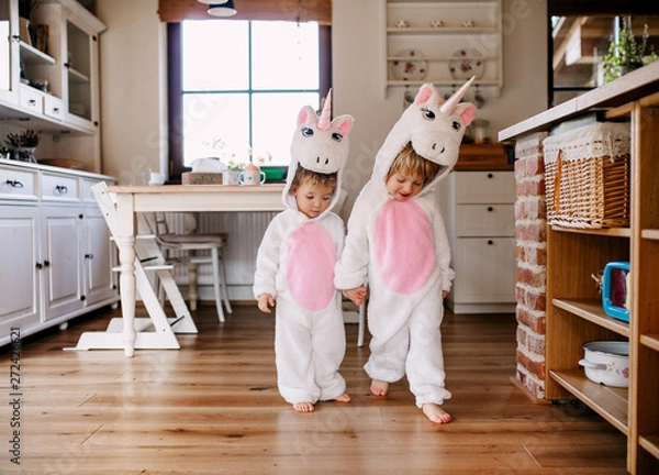 Fototapeta Two toddler children with unicorn masks walking indoors at home.