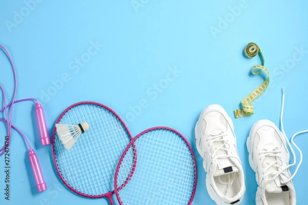 Fototapeta Sports flat lay with shuttlecock and badminton racket, skipping rope, sneakers and measuring tape on blue background. Fitness, sport and healthy lifestyle concept.