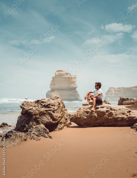 Fototapeta Tourist seated in a rock in a beach in the Twelve Apostles, near Melbourne, in Australia, with a bird near him