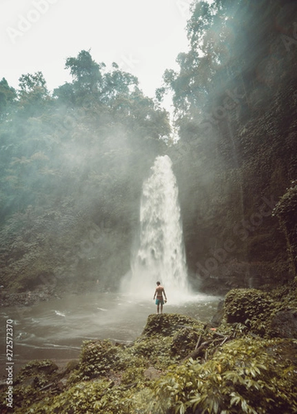 Fototapeta Guy alone in the middle of a huge waterfall in Bali, Indonesia