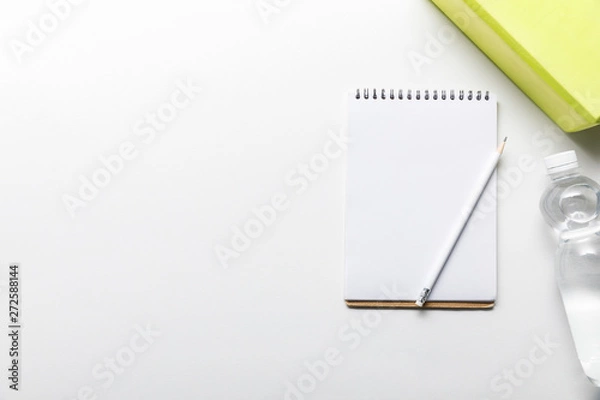 Fototapeta top view of water in bottle and blank notebook with pencil near box on white background