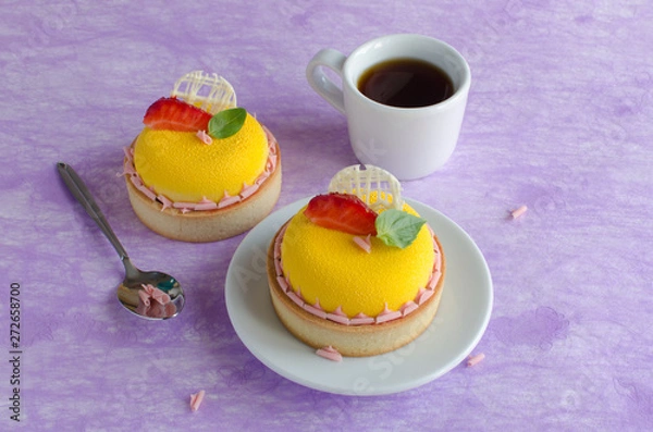 Fototapeta Contemporary tropical mini mousse tarts covered with yellow velvet spray decorated with fresh strawberries, basil and chocolate elements with cup of black tee on violet background