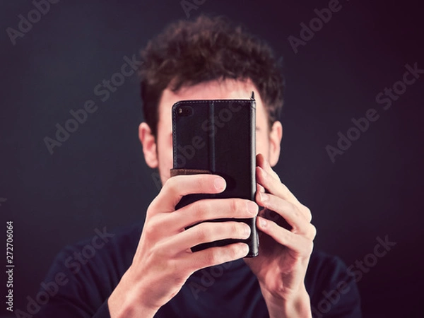 Obraz man with smartphone in front of face, front view of young person holding a mobile phone in hands (the Telephone covering his expression)