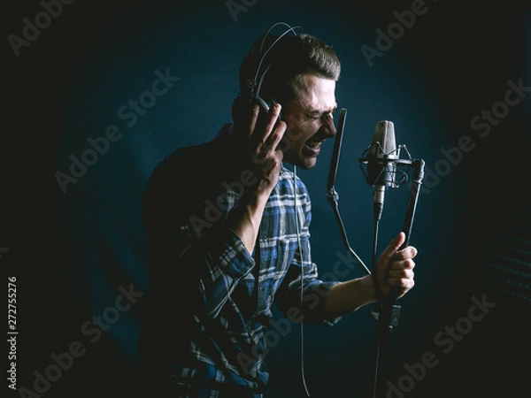 Fototapeta The young guy singing in recording studio