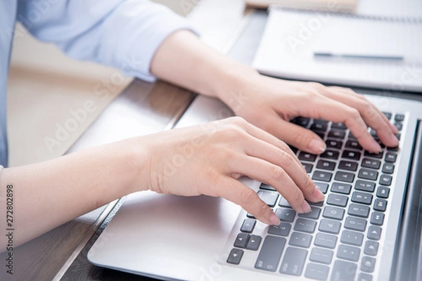 Fototapeta Business concept. Woman in blue shirt typing on computer with coffee on office table, backlighting, sun glare effect, close up, side view, copy space