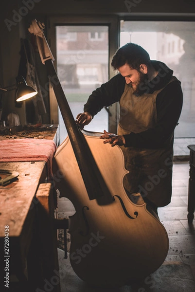 Obraz Young luthier working in his workshop, building a double bass