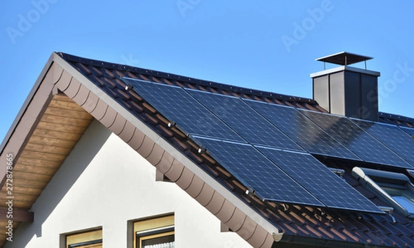 Fototapeta Solar panels installed on the roof of a house with tiles in Europe against the background of a blue sky. Green technology