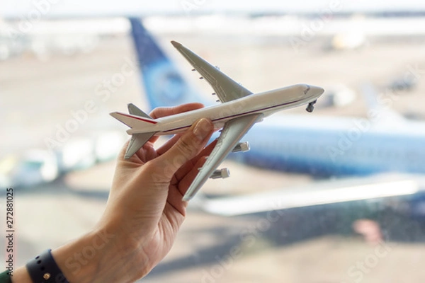 Fototapeta A girl holds a toy plane on the background of the airport. Concept on the theme of travel and freedom.