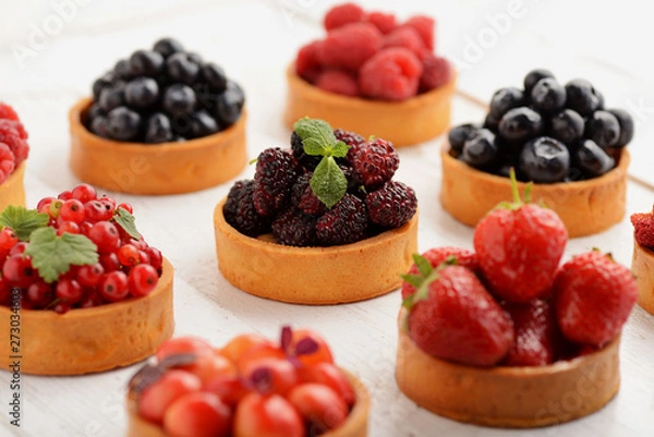 Obraz Fruit and berry tartlets dessert tray assorted . Beautiful delicious tarts, bright, colorful pastry cakes sweets with fresh raspberries, figs, strawberry. on white wooden background