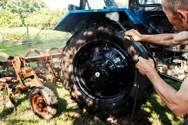 Obraz Man washes tractor wheels spraying pressure washer for tractor wash.
