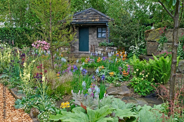 Fototapeta A country cottage and garden situated in a wooded rockery with a colourful display of flowers